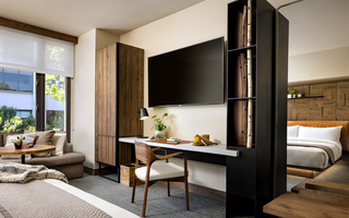 1 hotel sf guestroom bed facing the flat screen tv, custom built in desk, and a wooden storage cabinet