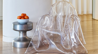 the mondrian clear acrylic chair next to a metal accent table will a bowl of oranges on top