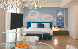 the mondrian king bed against a wall with clouds and two ring clouds in the sky. Hanging to the right of the bed is a mural of a girl swinging from a cloud in the middle of an open ocean