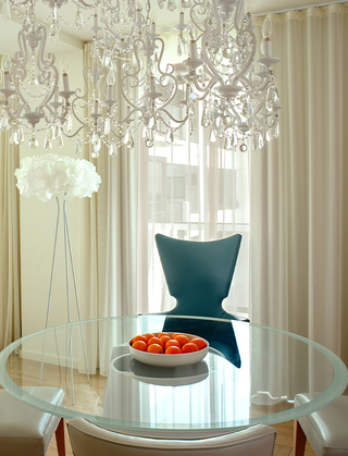 the mondrian crystal chandelier above a glass round table surrounded by a blue wingback chair and three beige wingback chairs on the other sides of the table in the suite
