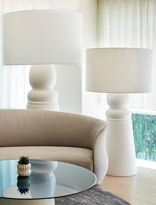 the mondrian lobby beige sofa with two large white floor lamps in the back and a round glass table in front