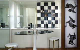 the mondrian suite mini bar with a sink, checkered floating wall shelf, and on the wall hangs a tall mural of a girl in 3 falling positions tumbling down the canvas