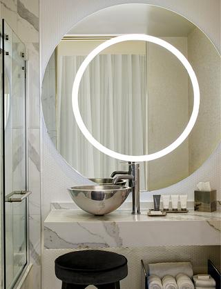 the mondrian round ring mirror on the wall and a silver vessel sink with marble counter tops in the bathroom