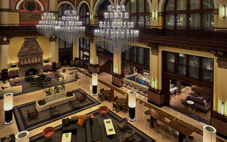 union station nashville lobby view from the second floor featuring the stone fireplace, sofas and table seating, the bar, and hanging from the ceiling is three large dazzling chandeliers
