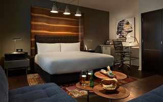 hotel zetta guestroom featuring the bed at center, nightstand to the left, and desk with painting of woman hanging above to the right