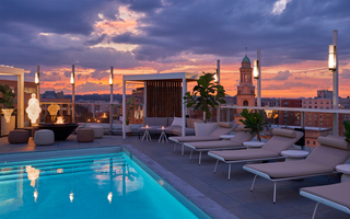 hotel zena outdoor pool with wood cabana, lounge chairs, firepit, and woman light sculpture is displayed to the right of the pool