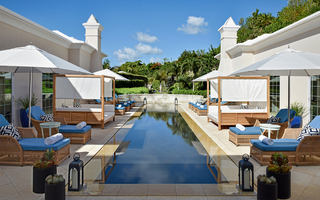 rosewood bermuda rectangular infinity pool at the center of a row of lounge seating and wooden cabanas