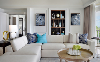 rosewood bermuda harbour court living room featuring an L shaped sofa next to a wooden coffee table. Behind the sofa and against the wall is a wooden storage unit in between two paintings of blue and white brush strokes on a black canvas
