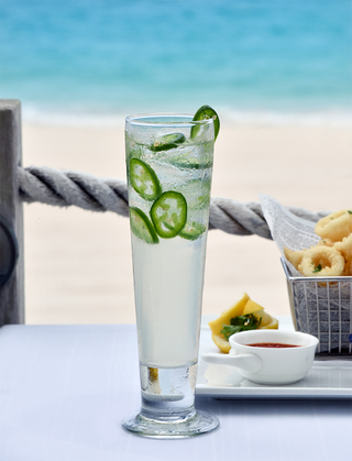 rosewood bermuda alcoholic beverage with jalapenos garnished on top with a basket of calamari to the right of the drink