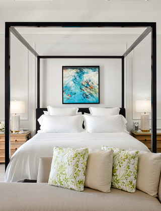 rosewood bermuda canopy bed with a beige ottoman bench at the foot of the bed and two wooden night stands on each side of the bed