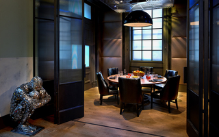 dirty habit dc glass folding doors leading into a reserved room with a round table and seating at center. In front of the folding doors, a metal sculpture in a fetal position sits in the corner