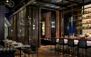 dirty habit dc metal silver top tables, leather tufted sofa, and leather chairs to the left and the corner of the bar to the right