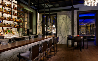 dirty habit dc bar with 5 tiers of liquor bottles on display and parallel to it is a long wooden bar table and brown leather high-top chairs at front