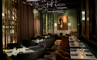 dirty habit dc dining area filled with armchairs, silver top tables, and long leather tufted seating running across the wall. In the background the bronze mural of a woman is on display