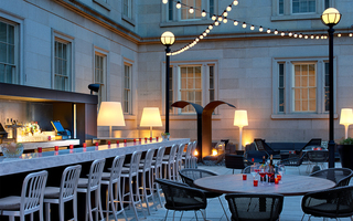 dirty habit dc outdoor bar with a spacious granite table and metal high top chairs to the left. To the right, patio seating and string of bulb lights hang from lamp posts that decorate the space