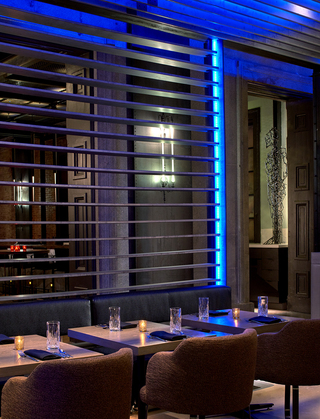dirty habit dc restaurant seating in front of a metal panel with a neon blue light reflecting off of it. In the distance, a metal statue stands on a cabinet