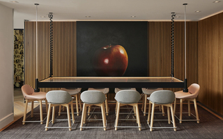hotel zena lobby pastel pink and grey chairs surround an industrial glass dining table hanging from the ceiling. Behind the table, a hyperrealistic red apple mural is hung on the wall