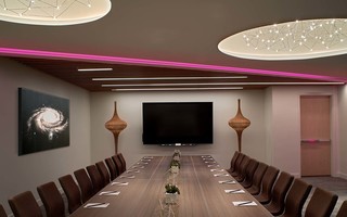 w la meeting room featuring a conference table, a tv hung on the wall, a mural of the milky way galaxy hung to the left, and two fairy light fixtures mounted on the ceiling