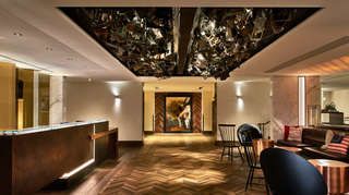 revere hotel reception desk to the left and lobby seating to the right. Up on the ceiling is a large rectangular light installation filled with numerous metal items grouped together in a cluster