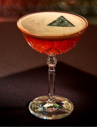 revere hotel amber colored martini with an illuminati symbol resting on top of the foam