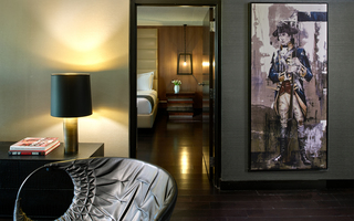 revere hotel guestroom living room featuring a painting of Paul Revere and in the adjoined room is a door view of the guestroom bed and wood nightstand