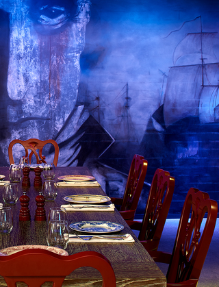 revere hotel rebel's guild wooden dining table with red chairs and a mural of sailboats and a man staring out into the dining room