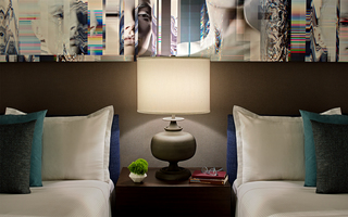 hotel zelos guestroom night stand with a psychedelic mural of a woman hanging above the twin beds