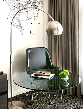 hotel zelos guestroom leather chair and round glass table beside a standing metal lamp