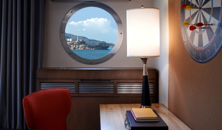 hotel zephyr guestroom desk with circular port hole window at center and dart board to the right hanging on the wall