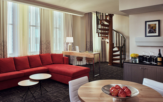 hotel vintage suite living room featuring a red sofa, desk, round wooden table seating, and stairs winding up to the bedroom
