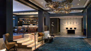 the logan lobby reception desk and stairs leading up to the lobby bar. Hanging from the ceiling is a large chandelier of framed photos of historical figures