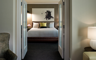 the logan guestroom swing doors revealing the king bed and a contemporary art piece of black brush strokes on a white canvas hanging above on the wall