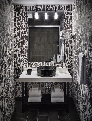 hotel zeppelin guestroom bathroom sink and rectangular mirror surrounded by wallpaper filled with band names across the walls