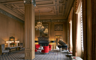 sir francis drake meeting area featuring a grand piano, decorated high ceilings, with a gold chandelier hanging above some seating by the fireplace mantel