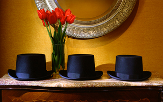 Kimpton hotel vintage seattle red tulips in a glass vase behind three black top hats lined up in a row on top of a console table