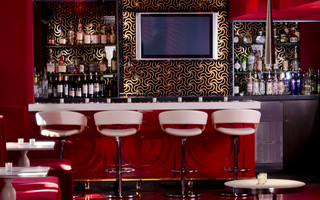 Bar rouge close up of the bar's high-top seating and in the back displays a black wall decorated with gold colored peppermint swirl patterns