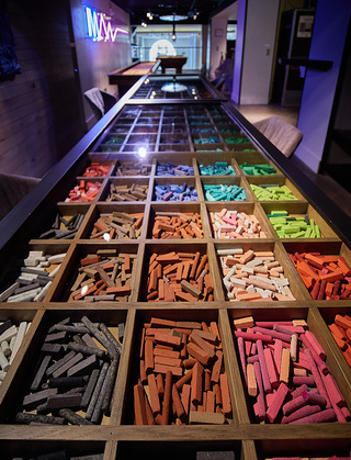 hotel zetta close up of the dining table that has a row of storage cubbies filled with colored pastels and incased with a hinged glass opening