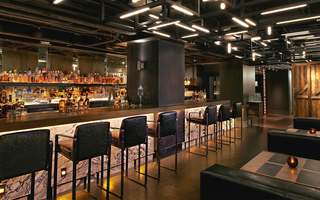 dirty habit sf long wooden bar top table featuring liquor bottles across the bar wall and an abundance of seating around the bar. Across the bar are leather booths for dining