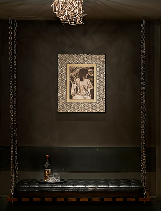 dirty habit sf black leather chair swing and on the wall hangs a mural of a woman lightly wrapped with white cloth around parts of her body and in hand, she holds a large feather fan